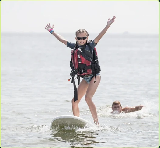 Young surfer standing on a surfboard with arms raised while riding a small wave.